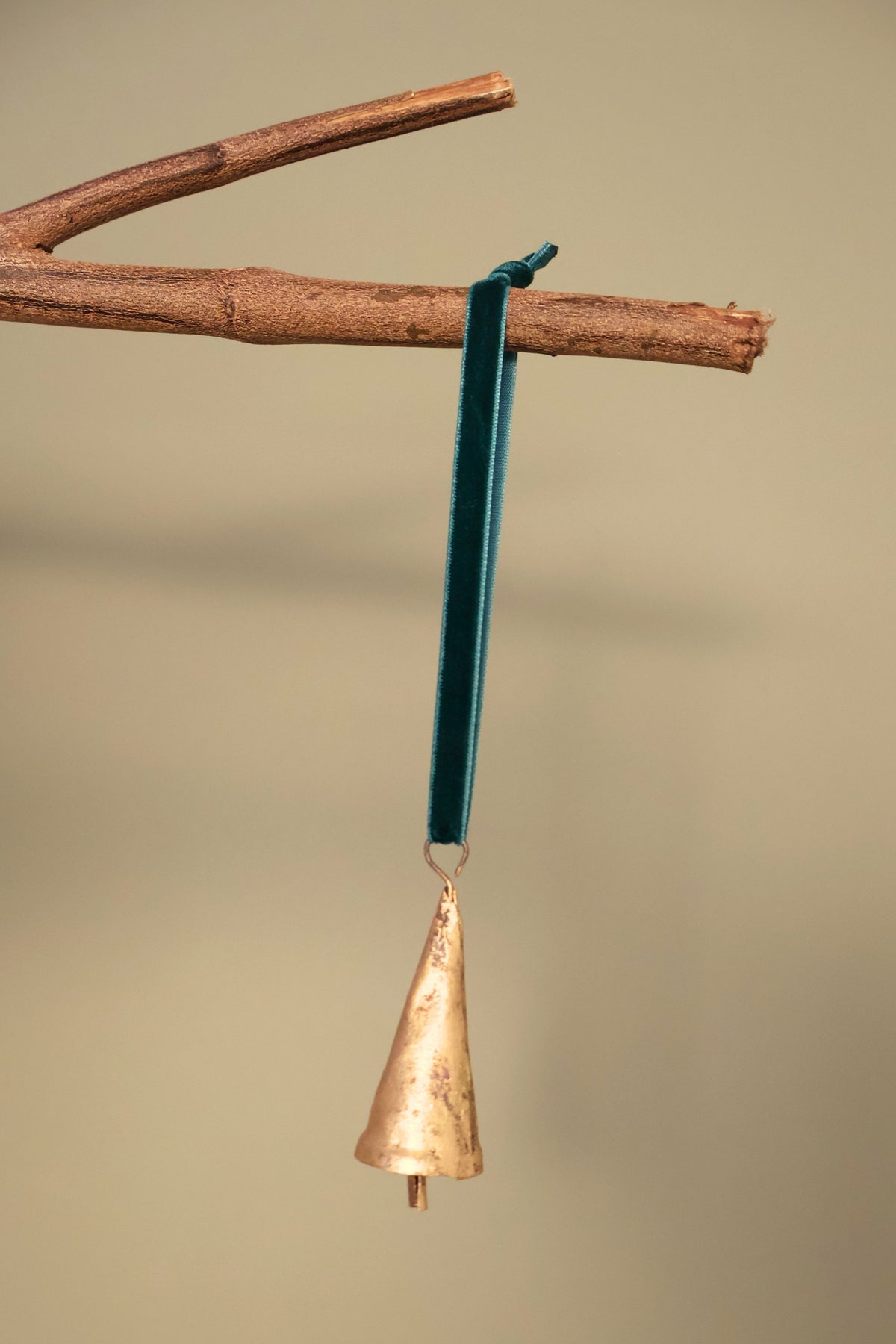 Bijou Rustic Cone Bell in antique gold hanging from a branch on an emerald green velvet ribbon