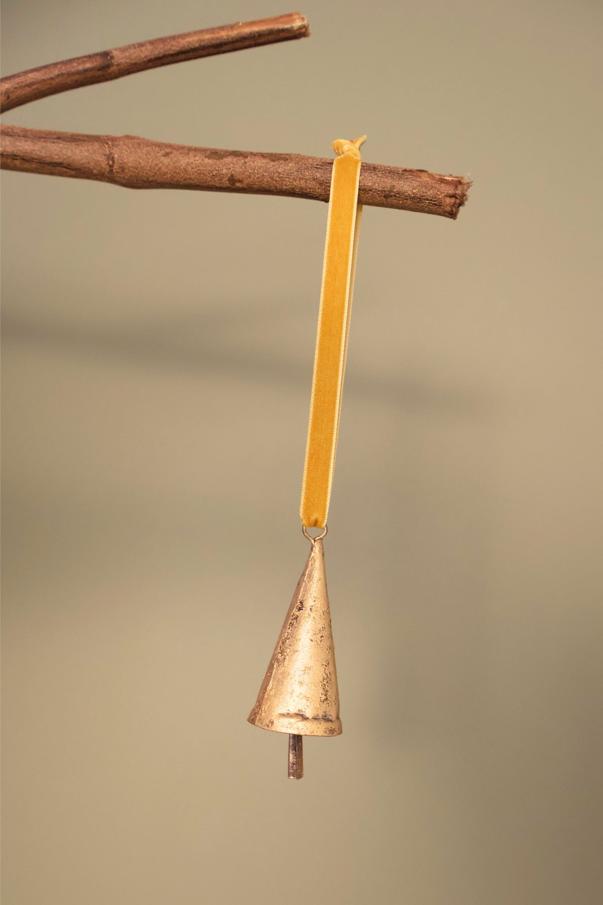 Bijou Rustic Cone Bell in antique gold hanging from a branch on an antique gold velvet ribbon