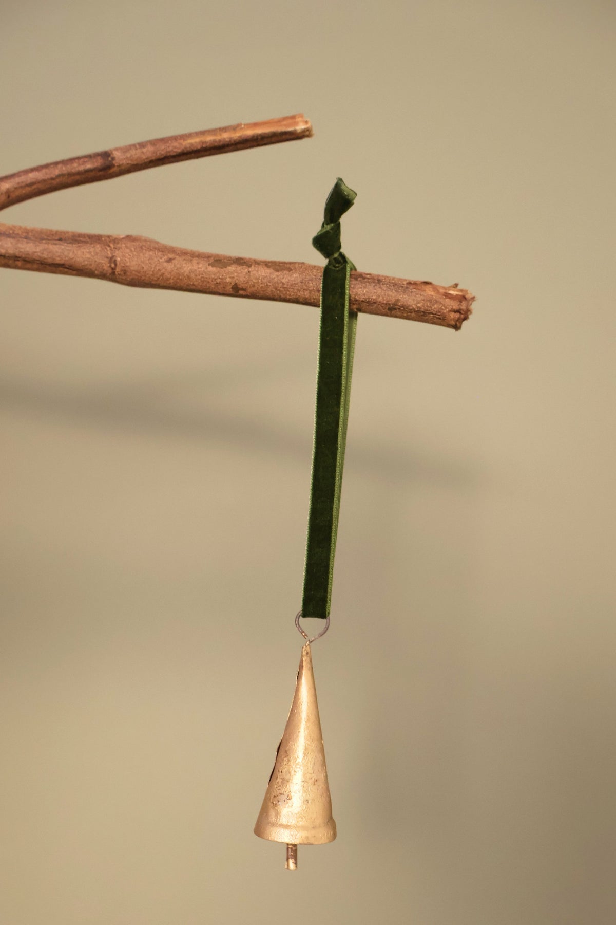 Bijou Rustic Cone Bell in antique gold hanging from a branch on an olive green velvet ribbon