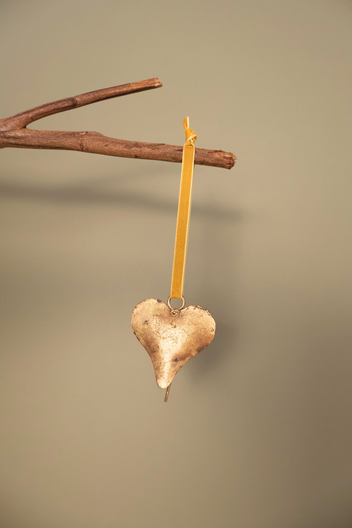 Bijou Rustic Heart Bell in antique gold hanging from a branch on an antique gold velvet ribbon