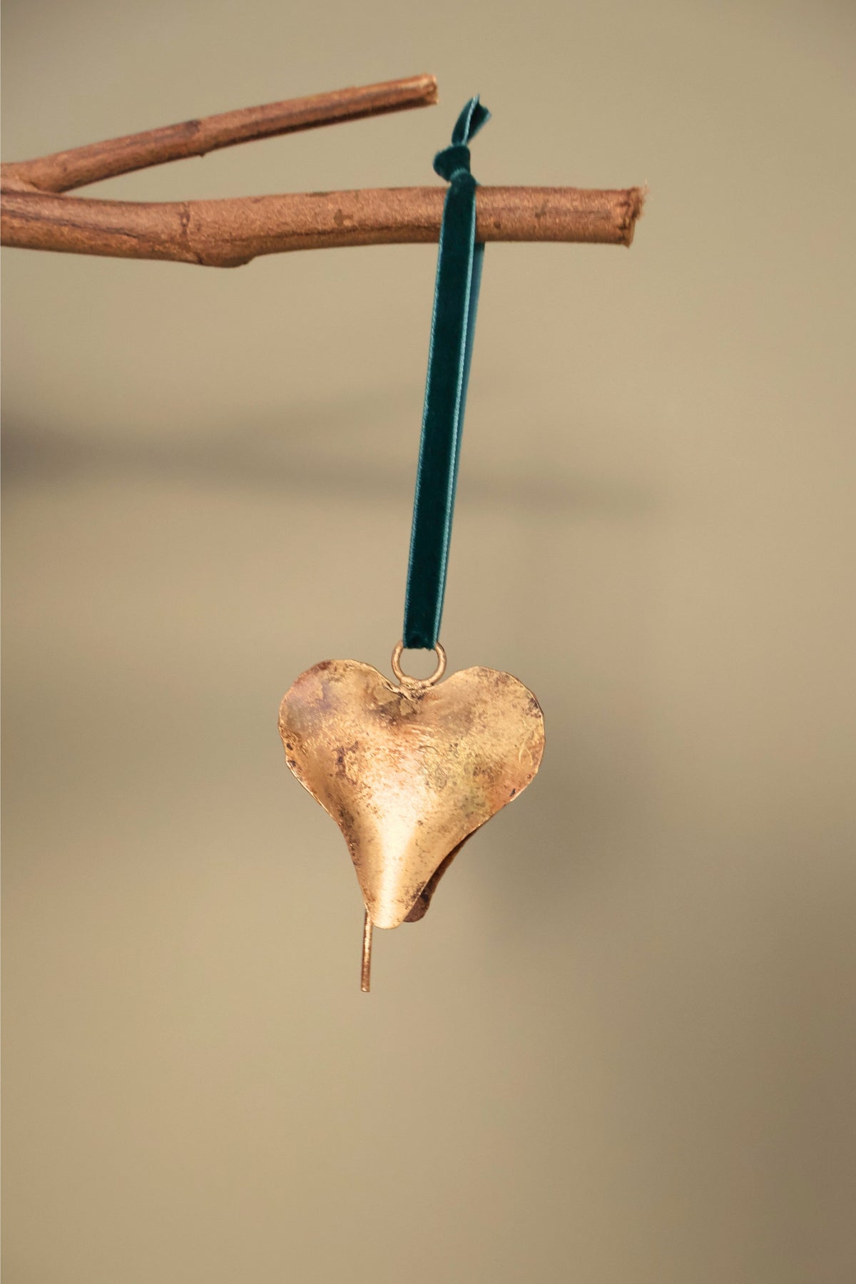 Bijou Rustic Heart Bell in antique gold hanging from a branch on an emerald green velvet ribbon