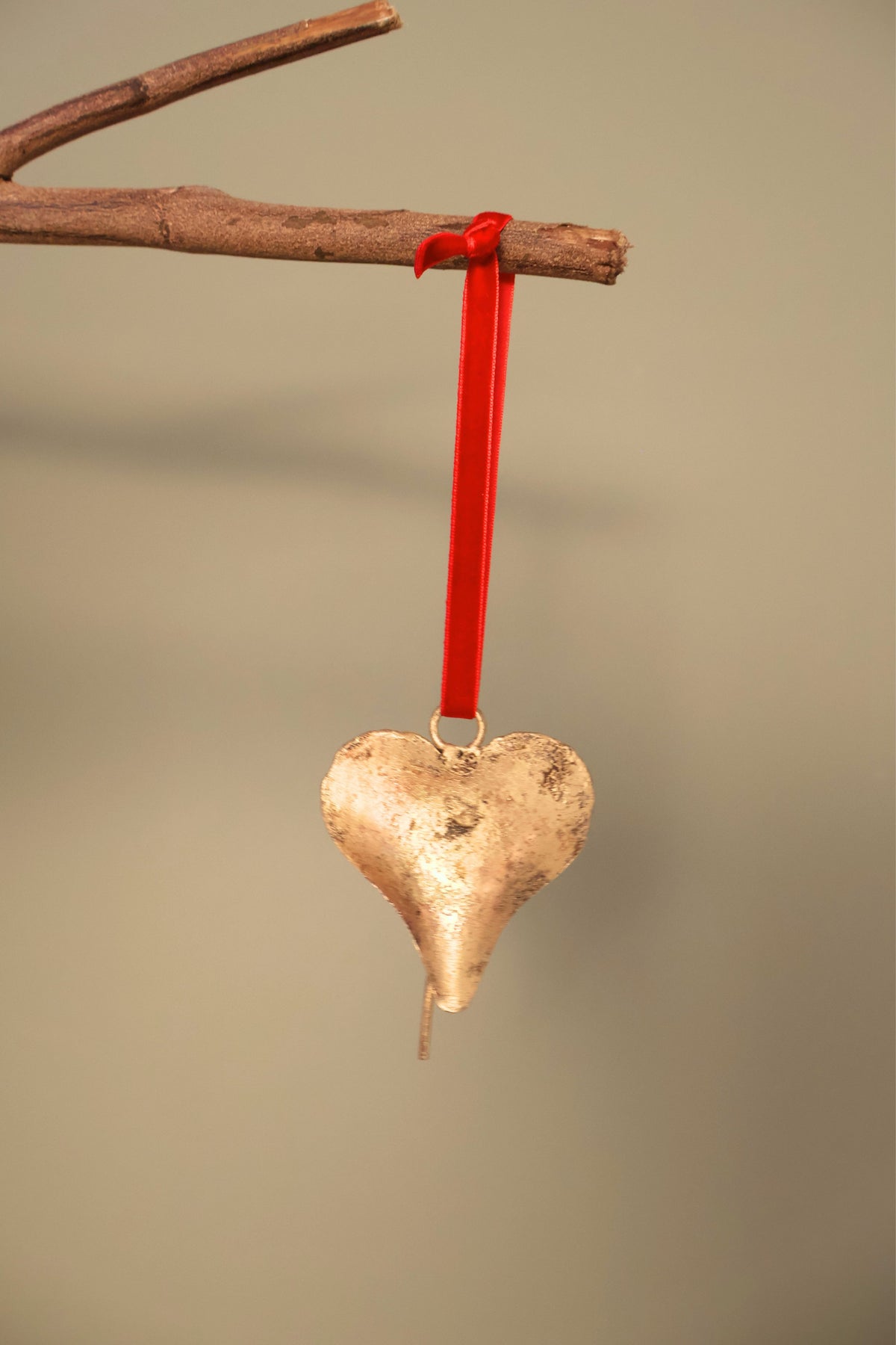 Bijou Rustic Heart Bell in antique gold hanging from a branch on a holly red velvet ribbon