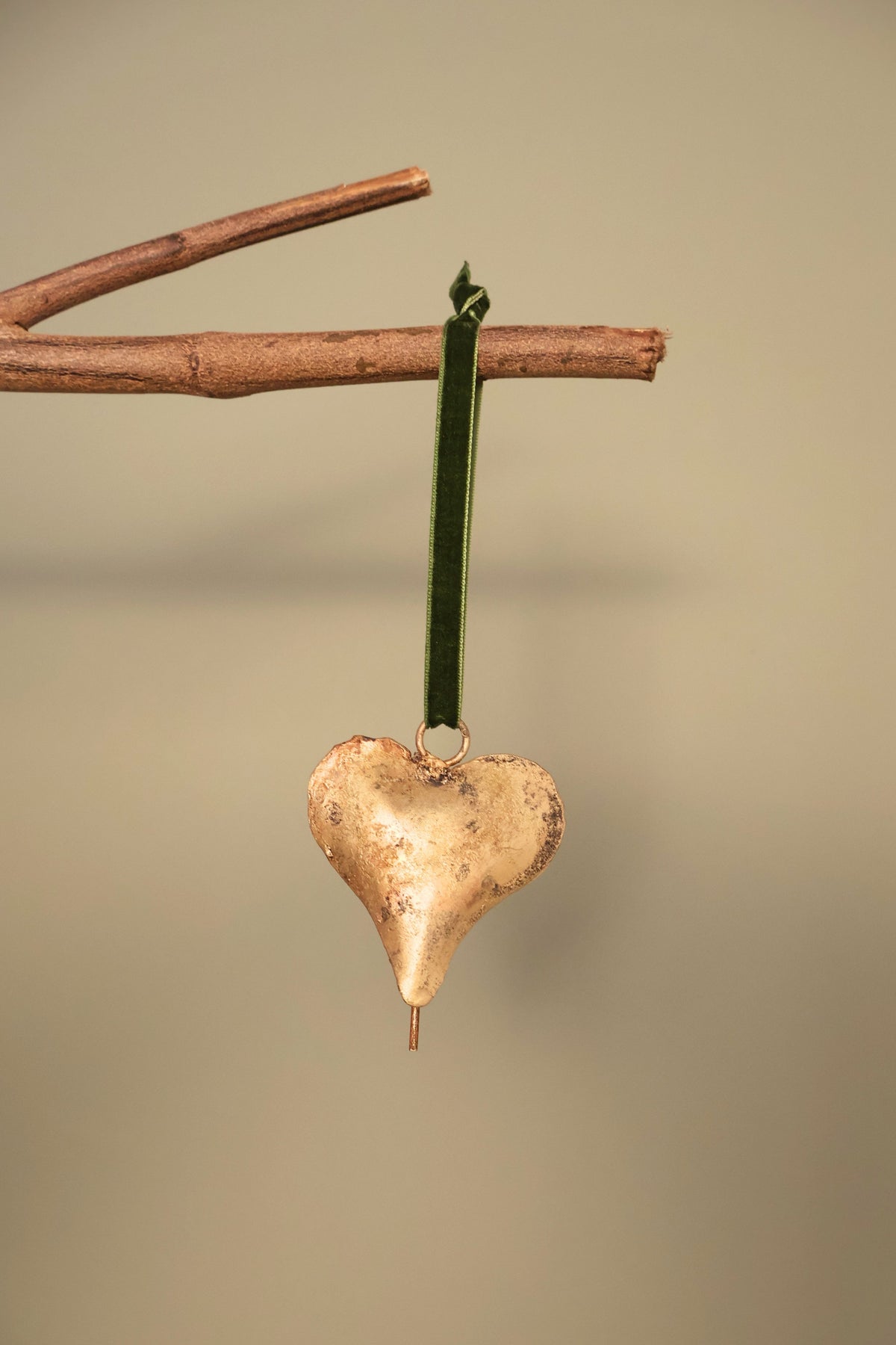 Bijou Rustic Heart Bell in antique gold hanging from a branch on an olive green velvet ribbon