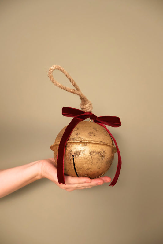 Bijou Rustic Jingle Bell, Large, held in a hand with a Bordeaux velvet ribbon bow and natural jute loop
