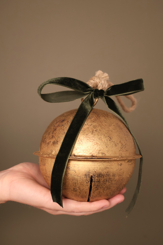 Bijou Rustic Jingle Bell, Large, held in a hand with a forest green velvet ribbon bow and natural jute loop