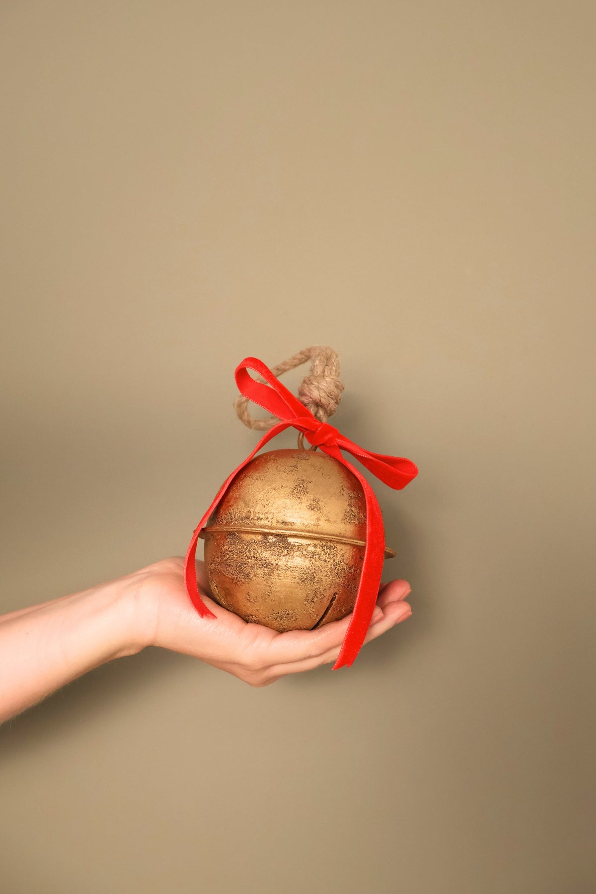 Bijou Rustic Jingle Bell, Medium, held in a hand with a classic red velvet ribbon bow and natural jute loop