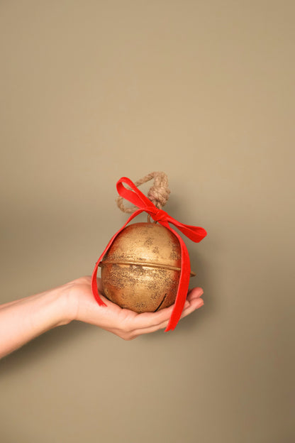 Bijou Rustic Jingle Bell, Medium, held in a hand with a classic red velvet ribbon bow and natural jute loop