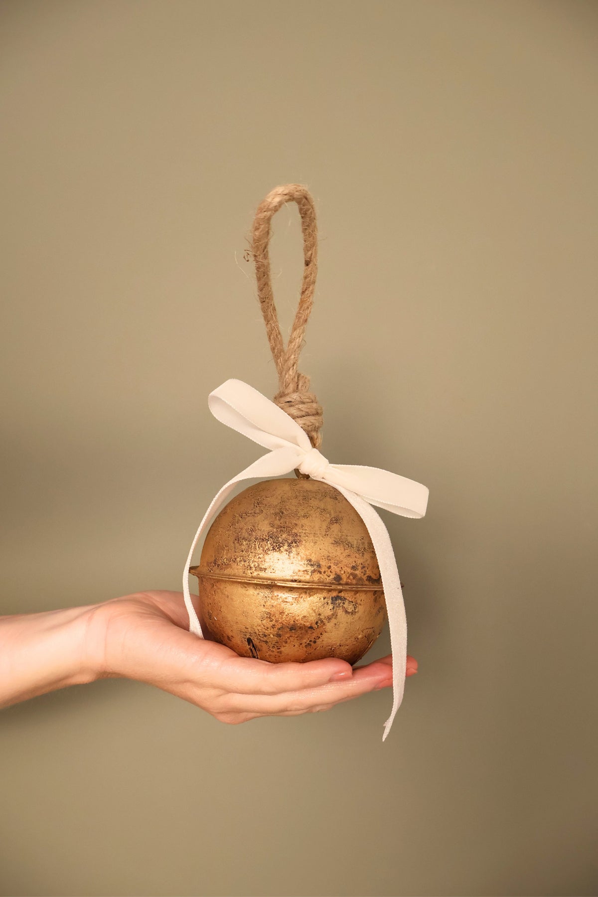 Bijou Rustic Jingle Bell, Medium, held in a hand with a cream velvet ribbon bow and natural jute loop
