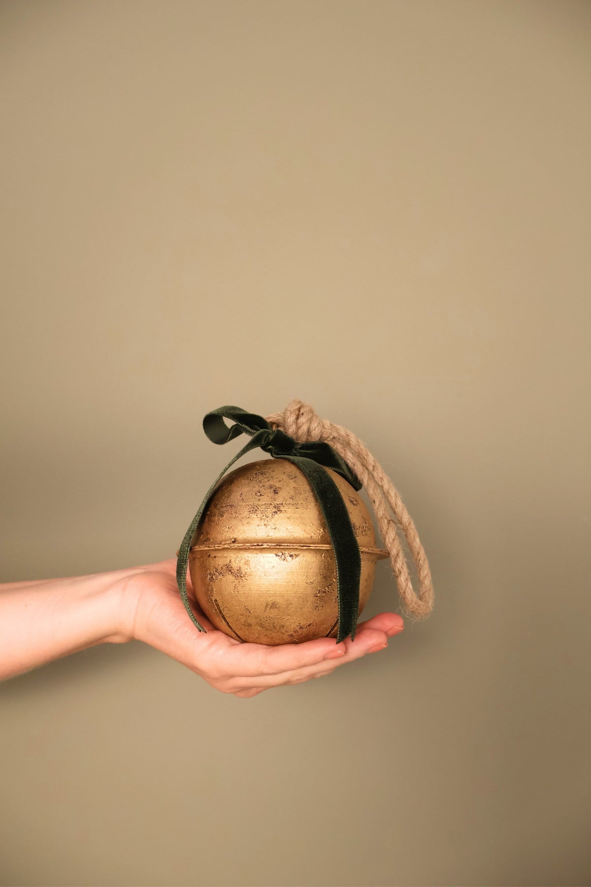 Bijou Rustic Jingle Bell, Medium, held in a hand with a forest green velvet ribbon bow and natural jute loop