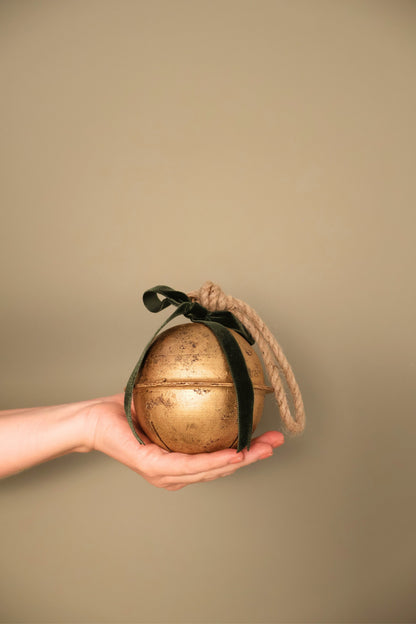 Bijou Rustic Jingle Bell, Medium, held in a hand with a forest green velvet ribbon bow and natural jute loop
