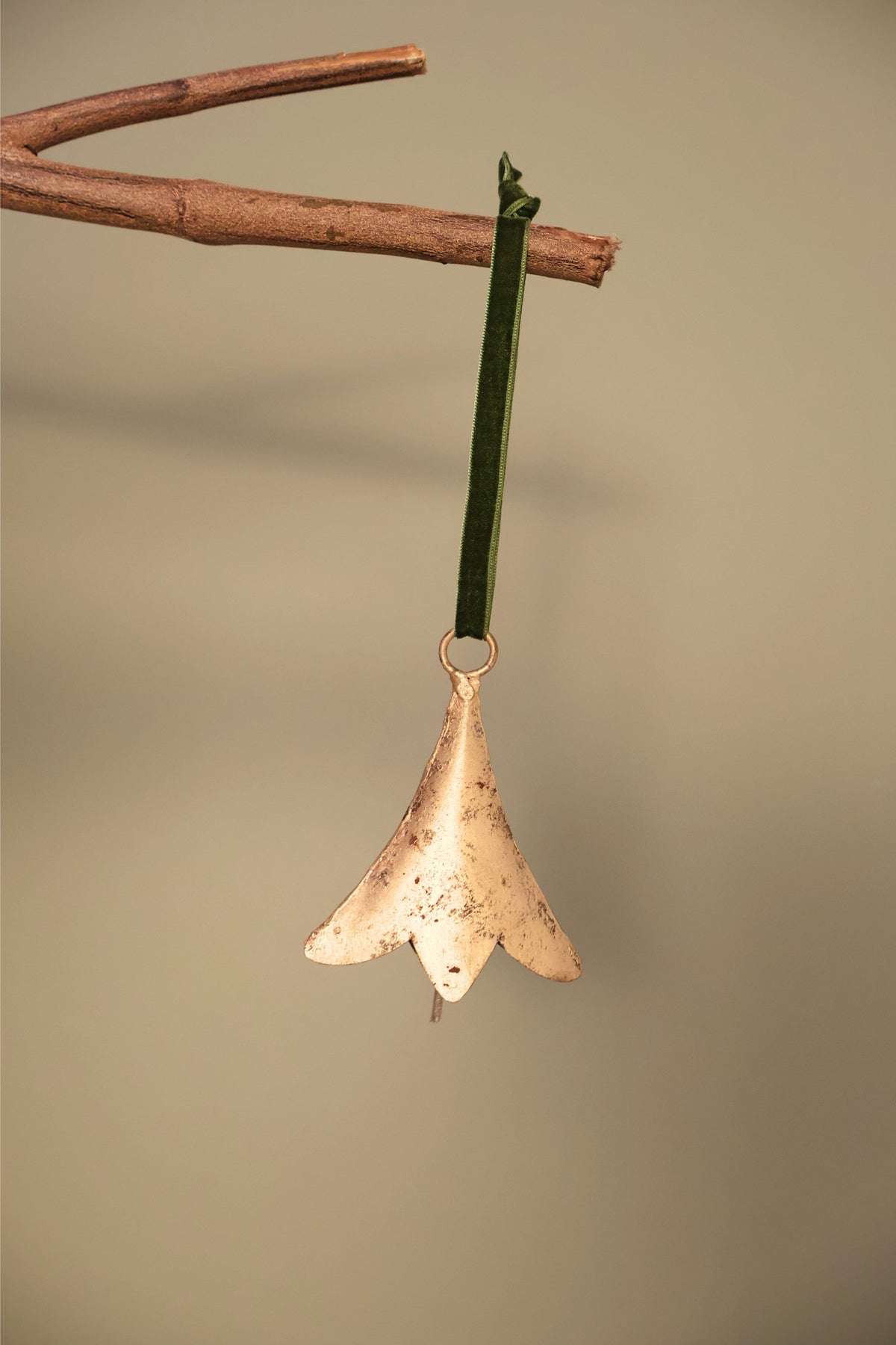 Bijou Rustic Scallop Bell in antique gold hanging from a branch on an olive green velvet ribbon