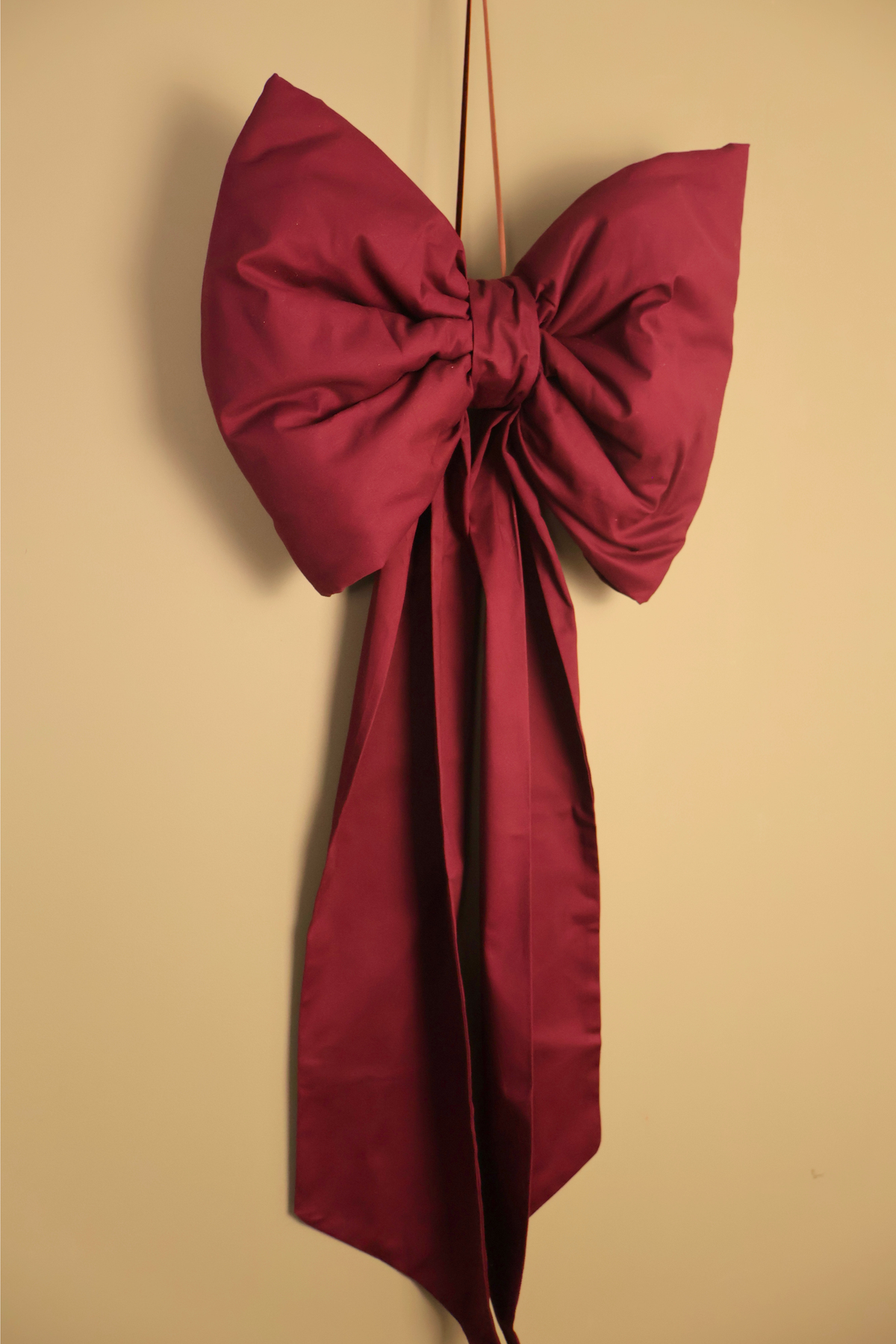 Burgundy handmade oversized cotton bow with long tails, hanging against a cream wall