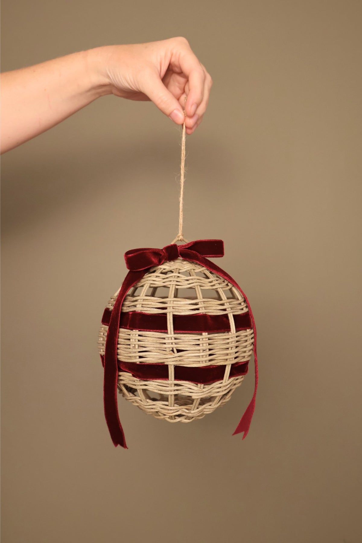Noël rattan bauble with a bordeaux velvet ribbon bow, hanging from a jute cord