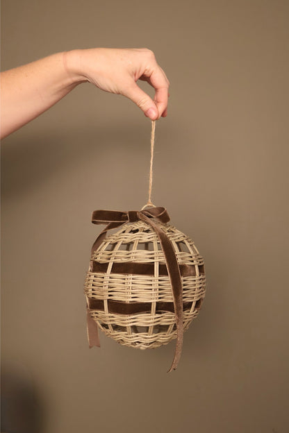 Noël rattan bauble with a chocolate velvet ribbon bow, hanging from a jute cord