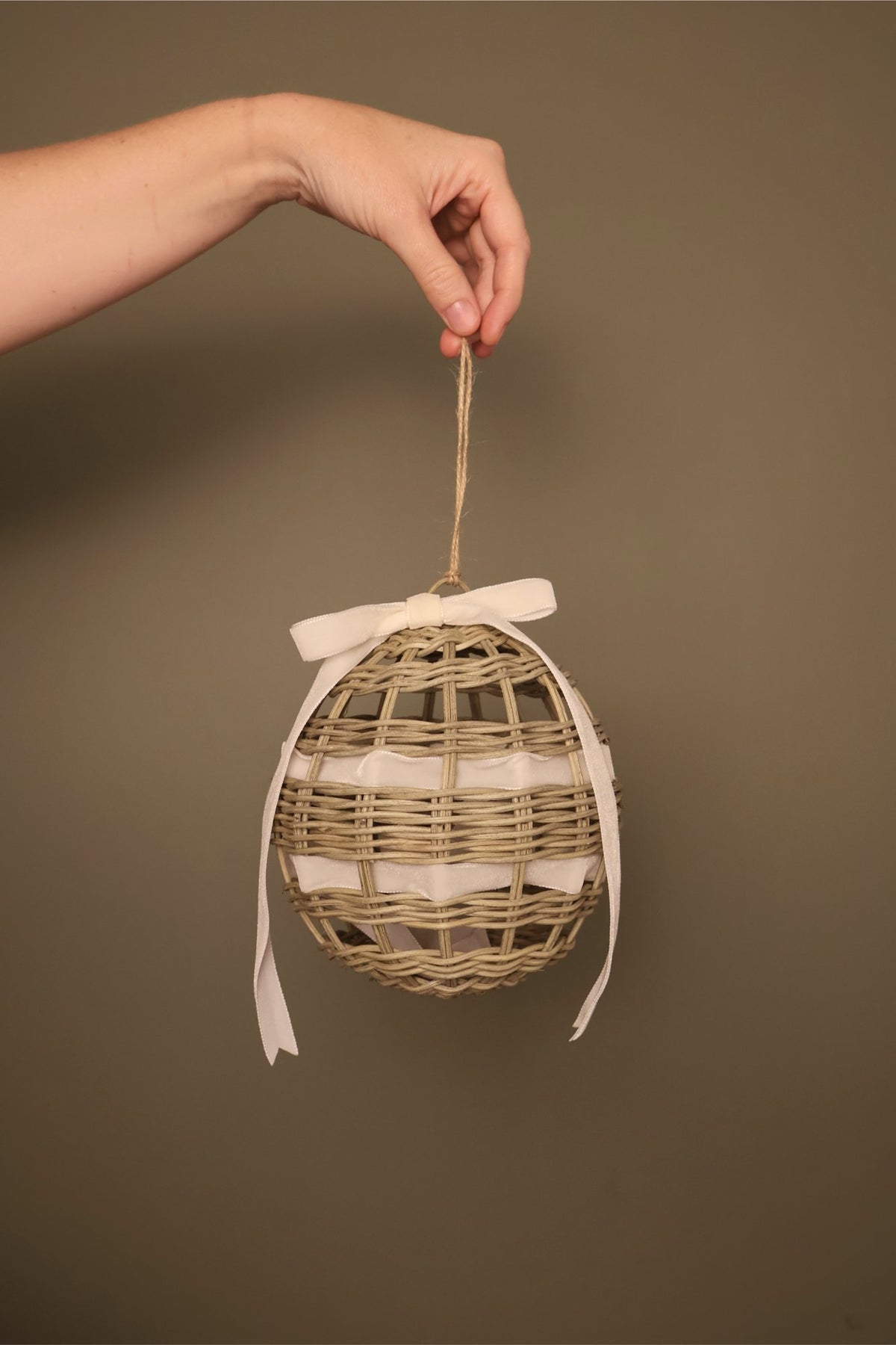 Noël rattan bauble with a cream velvet ribbon bow, hanging from a jute cord