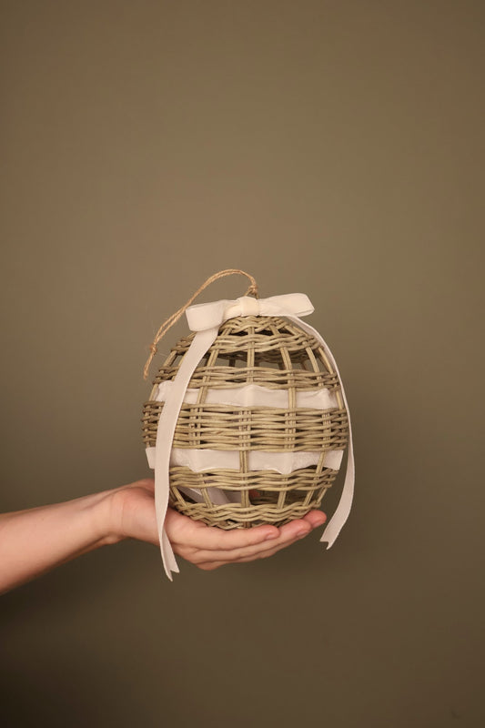 Noël rattan bauble with a cream velvet ribbon bow, held in a hand