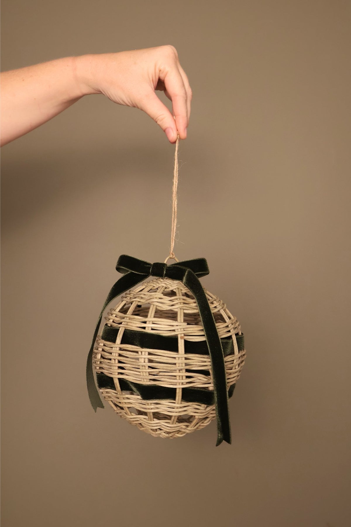 Noël rattan bauble with a forest green velvet ribbon bow, hanging from a jute cord