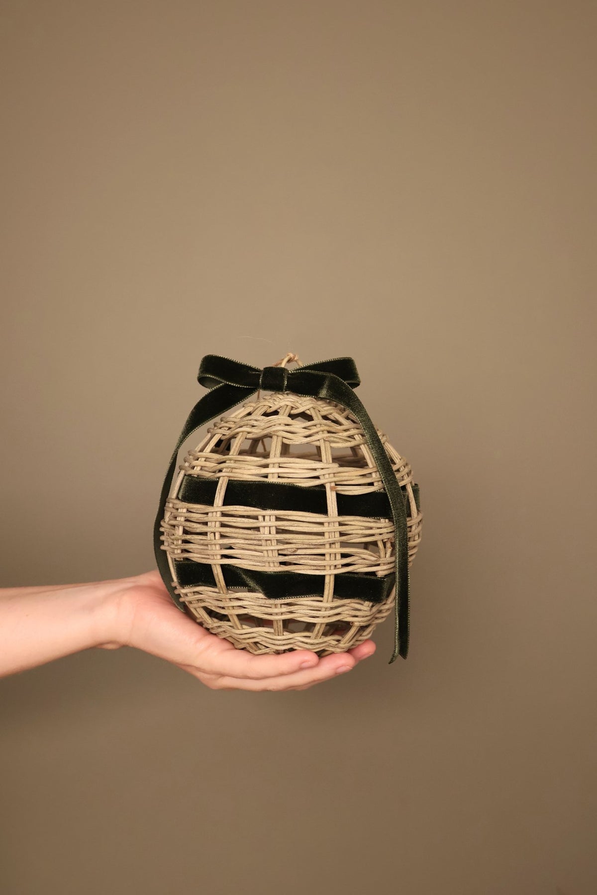 Noël rattan bauble with a forest green velvet ribbon bow, held in a hand