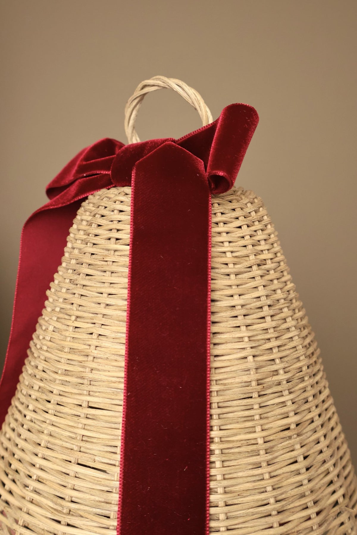 Close-up of a large Noël rattan bell with a bordeaux velvet ribbon bow and long ribbon tail