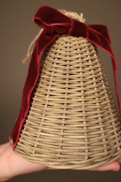 Close-up of a medium Noël rattan bell with a bordeaux velvet ribbon bow and long ribbon tails