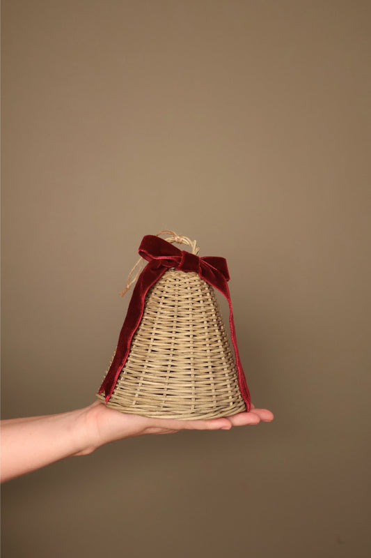 Medium Noël rattan bell with a bordeaux velvet ribbon bow and jute loop, held in a hand