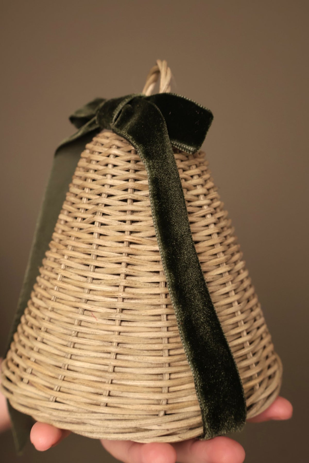 Close-up of a medium Noël rattan bell with a forest green velvet ribbon bow tied at the jute hanging loop