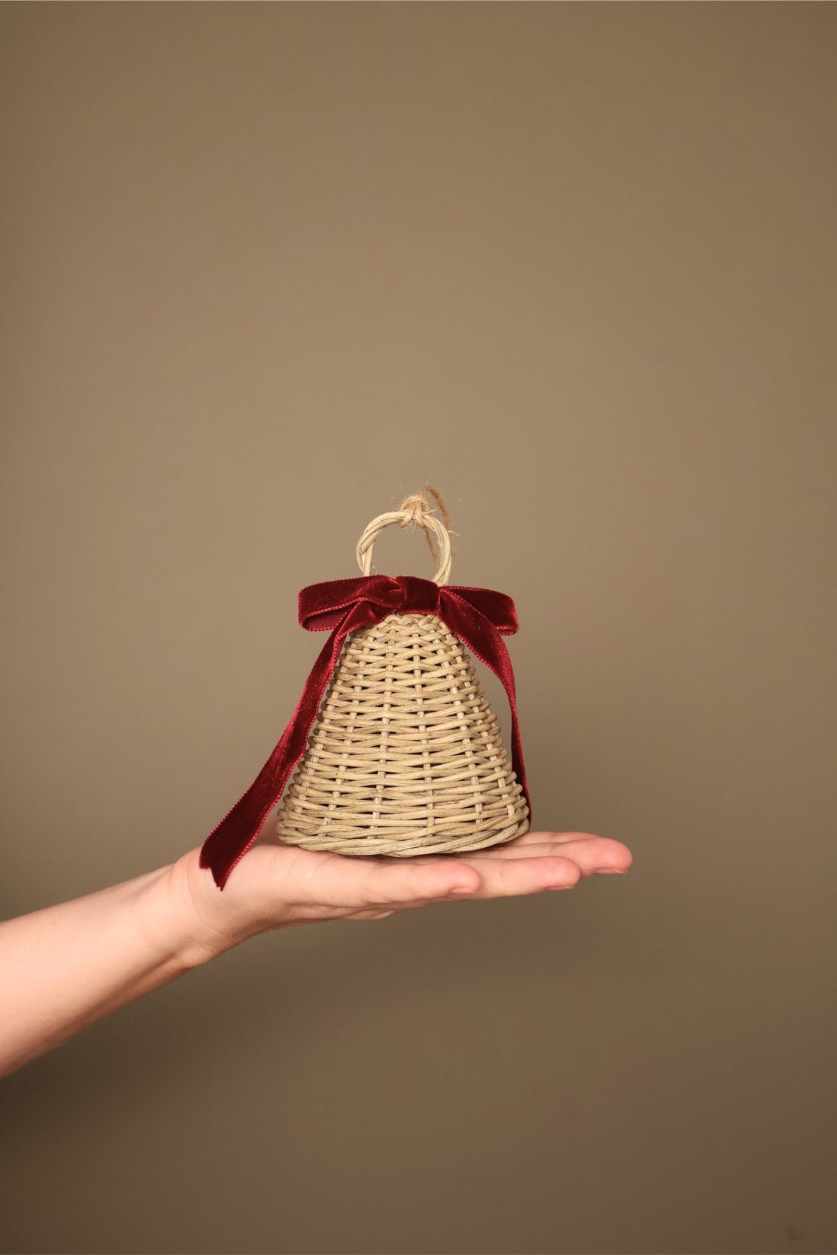 Small Noël rattan bell with a bordeaux velvet ribbon bow and jute loop, held in a hand