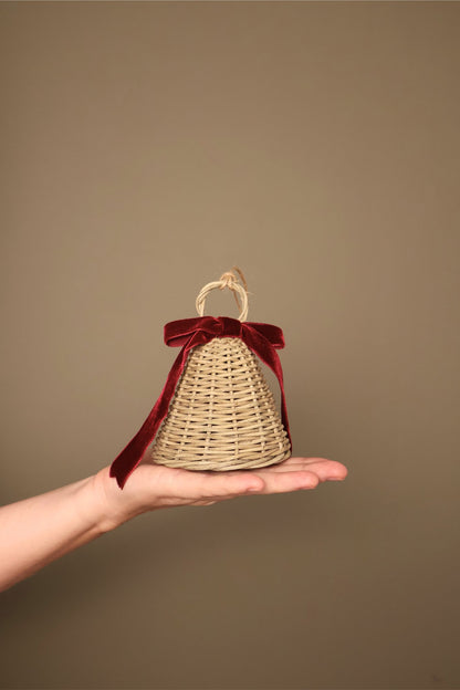 Small Noël rattan bell with a bordeaux velvet ribbon bow and jute loop, held in a hand