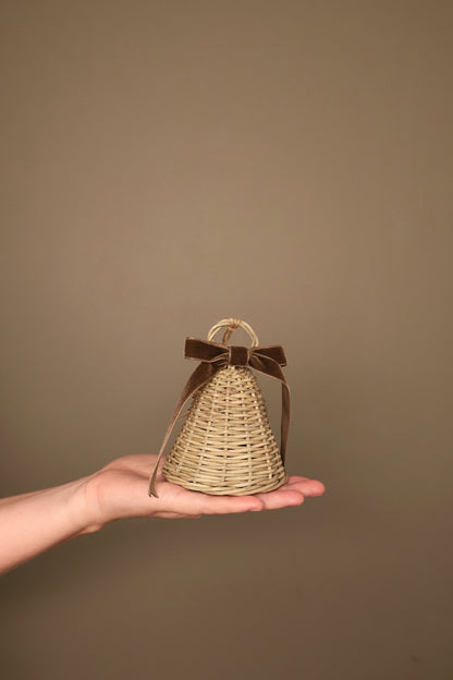 Small Noël rattan bell with a chocolate velvet ribbon bow and jute loop, held in a hand