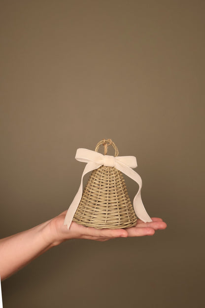 Small Noël rattan bell with a cream velvet ribbon bow and jute loop, held in a hand