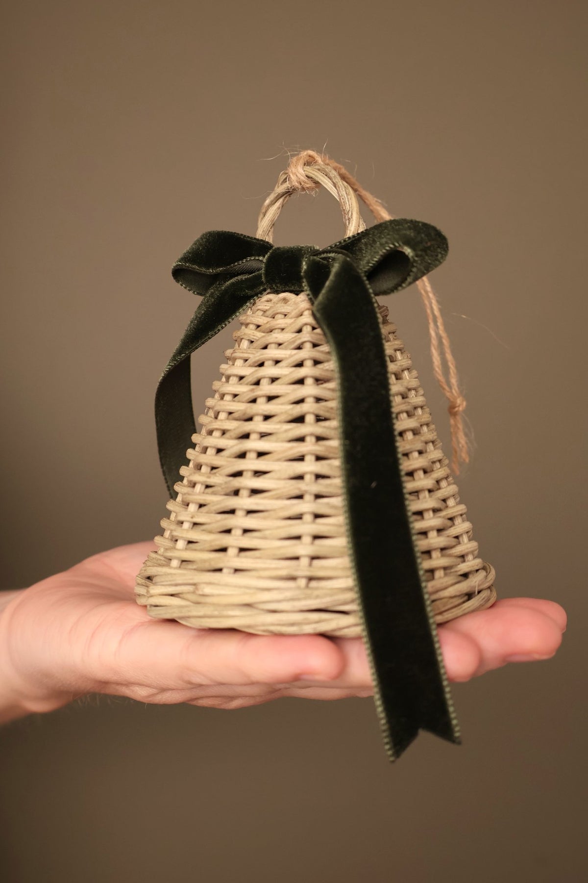 Close-up of a small Noël rattan bell with a forest green velvet ribbon bow and a jute hanging loop