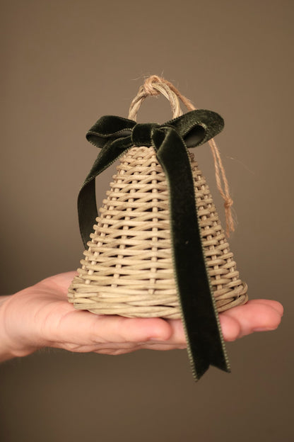 Close-up of a small Noël rattan bell with a forest green velvet ribbon bow and a jute hanging loop