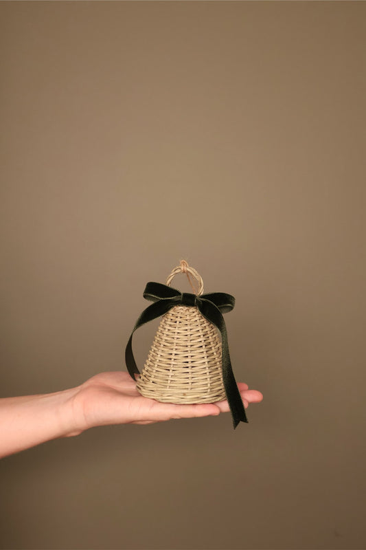 Small Noël rattan bell with a forest green velvet ribbon bow and jute loop, held in a hand